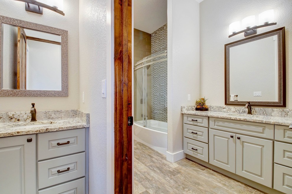 Photo of a large transitional master bathroom in Denver with raised-panel cabinets, white cabinets, brown tile, multi-coloured tile, mosaic tile, granite benchtops, multi-coloured benchtops, an alcove tub, a shower/bathtub combo, white walls, porcelain floors, an undermount sink, beige floor and a sliding shower screen.
