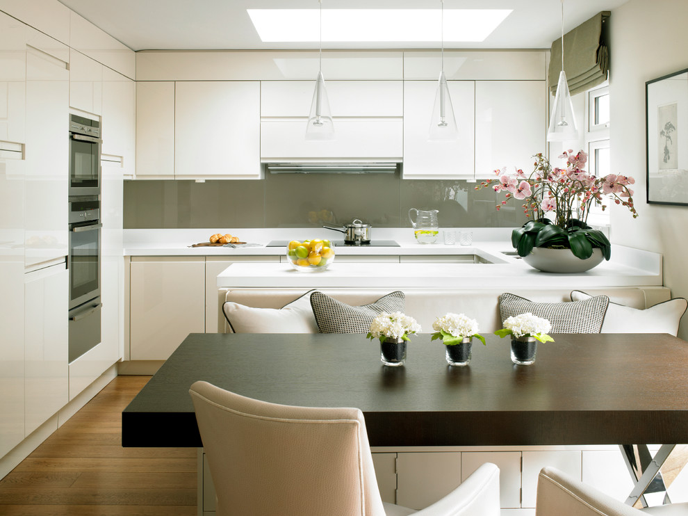 Inspiration for a contemporary u-shaped eat-in kitchen in London with flat-panel cabinets, white cabinets, grey splashback, glass sheet splashback and stainless steel appliances.