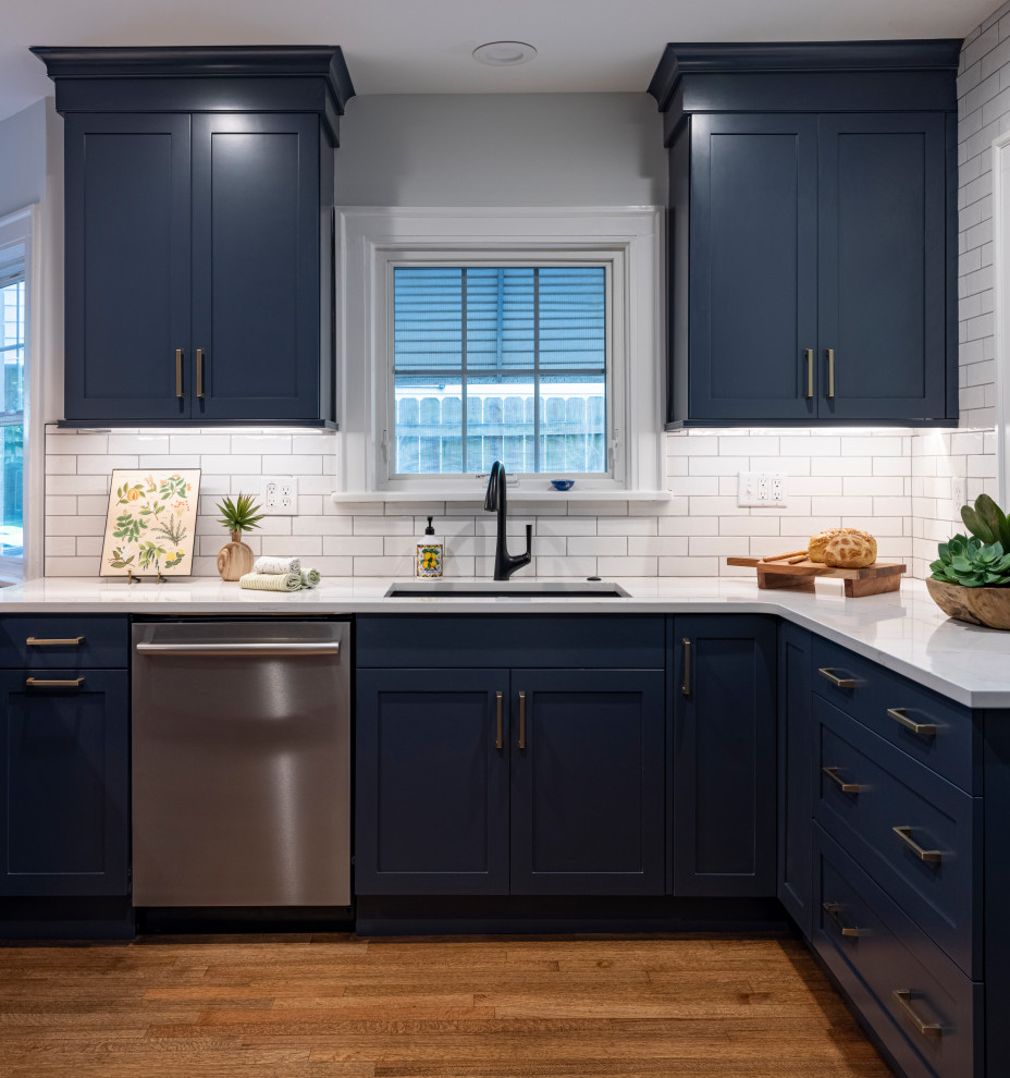 Inspiration for a small arts and crafts u-shaped kitchen pantry in Kansas City with an undermount sink, shaker cabinets, blue cabinets, quartz benchtops, white splashback, subway tile splashback, stainless steel appliances, medium hardwood floors, a peninsula, brown floor and white benchtop.