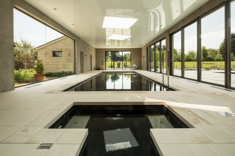 Large modern indoor rectangular lap pool in Hampshire with a pool house and natural stone pavers.