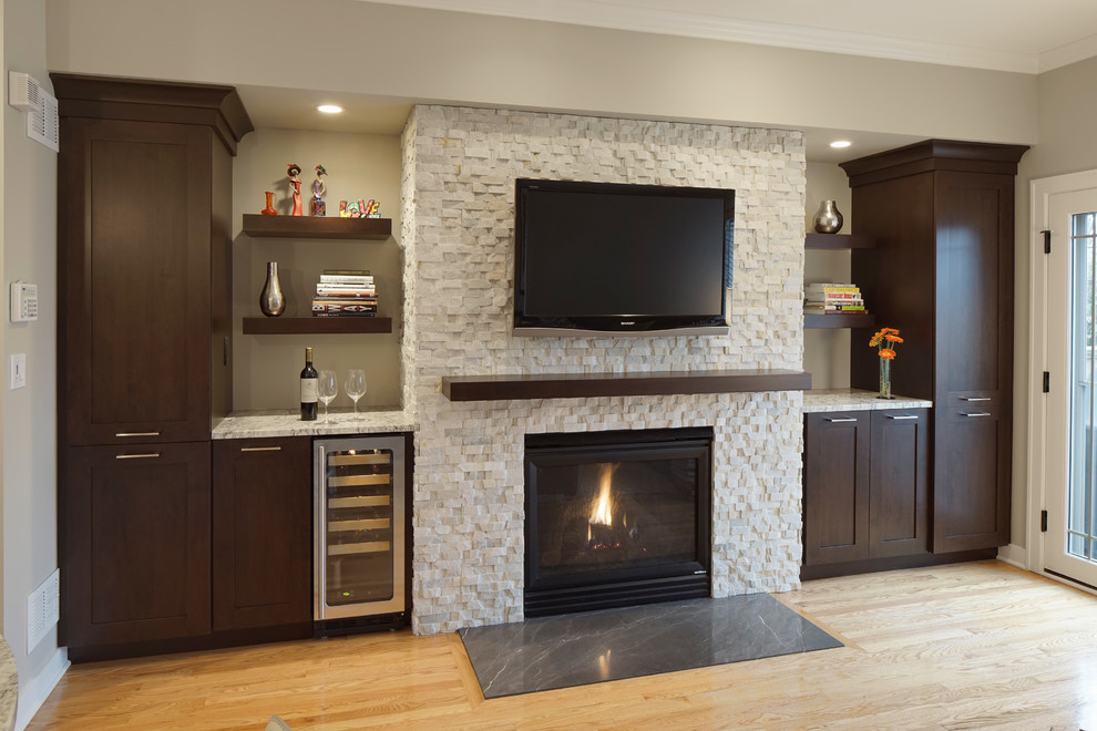 This is an example of a small transitional family room in Chicago with a home bar, grey walls, light hardwood floors, a stone fireplace surround and a wall-mounted tv.