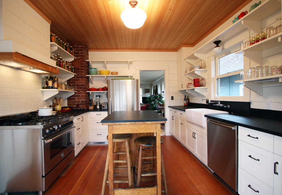 Photo of a traditional u-shaped separate kitchen in Portland with a farmhouse sink, white cabinets, shaker cabinets, solid surface benchtops, white splashback, medium hardwood floors and with island.