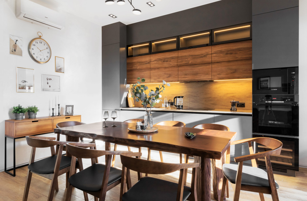 Идея дизайна: прямая кухня в современном стиле с обеденным столом, плоскими фасадами, серыми фасадами, черной техникой, паркетным полом среднего тона, коричневым полом и белой столешницей без острова