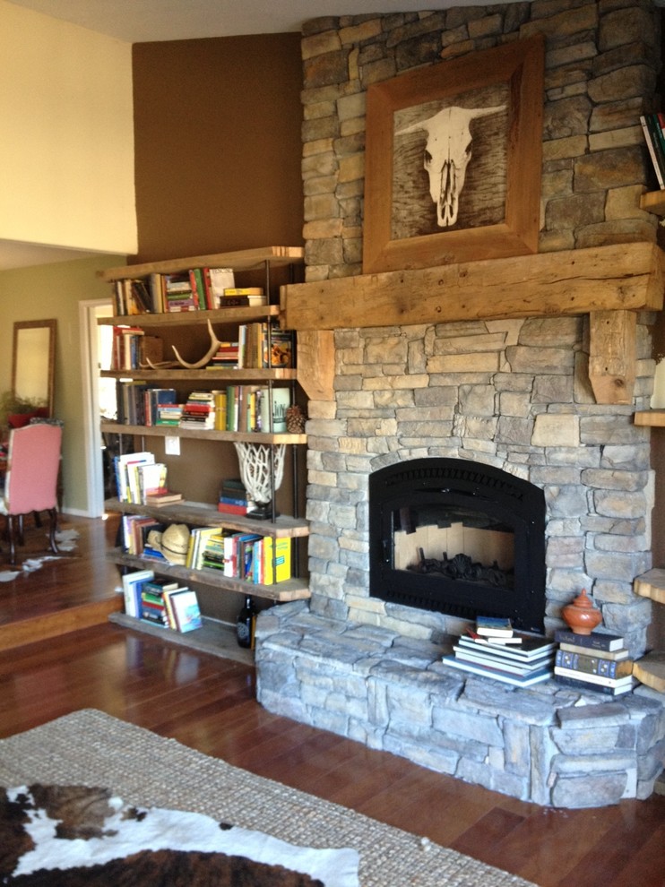 This is an example of a small country living room in San Luis Obispo with a library, brown walls, a wood stove and a stone fireplace surround.