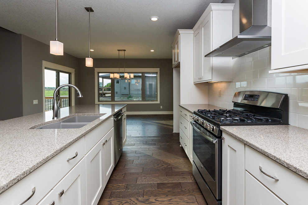 Inspiration for a transitional l-shaped dark wood floor open concept kitchen remodel with an undermount sink, shaker cabinets, white cabinets, quartz countertops, white backsplash, subway tile backsplash, stainless steel appliances and an island