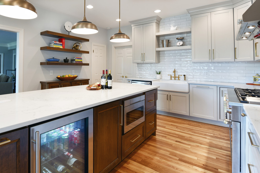 Inspiration for a large l-shaped medium tone wood floor and beige floor eat-in kitchen remodel in DC Metro with a farmhouse sink, recessed-panel cabinets, gray cabinets, quartz countertops, white backsplash, porcelain backsplash, stainless steel appliances, an island and white countertops