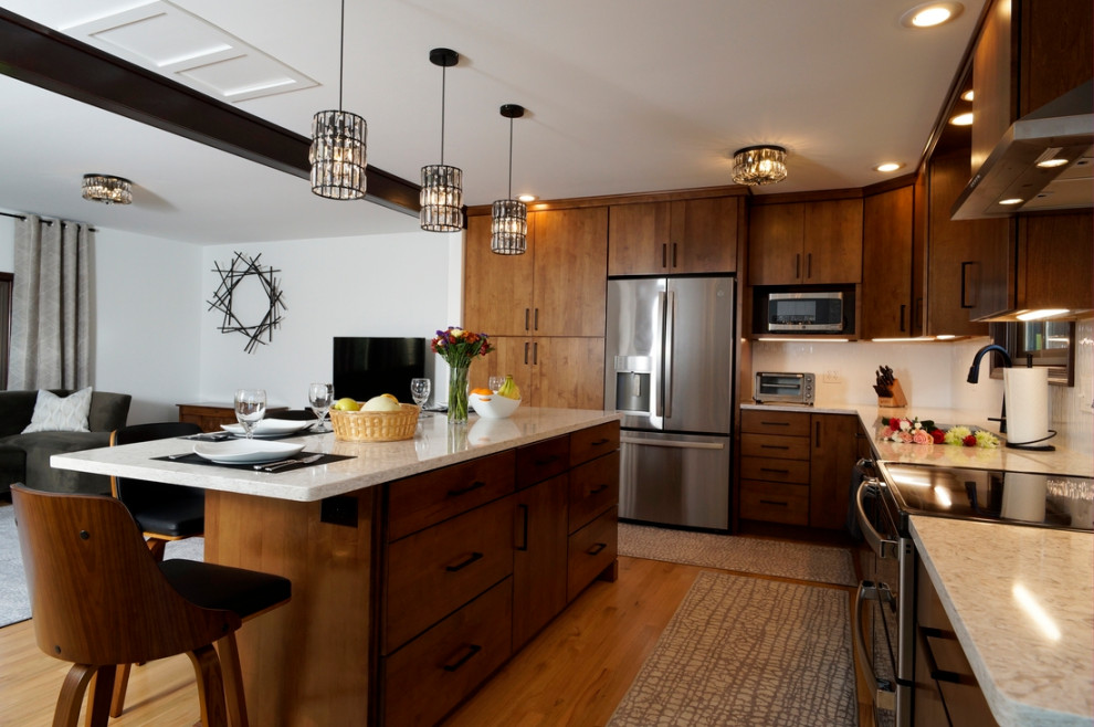 Photo of a mid-sized modern l-shaped eat-in kitchen in Philadelphia with a double-bowl sink, flat-panel cabinets, medium wood cabinets, quartz benchtops, white splashback, porcelain splashback, stainless steel appliances, light hardwood floors, with island and white benchtop.