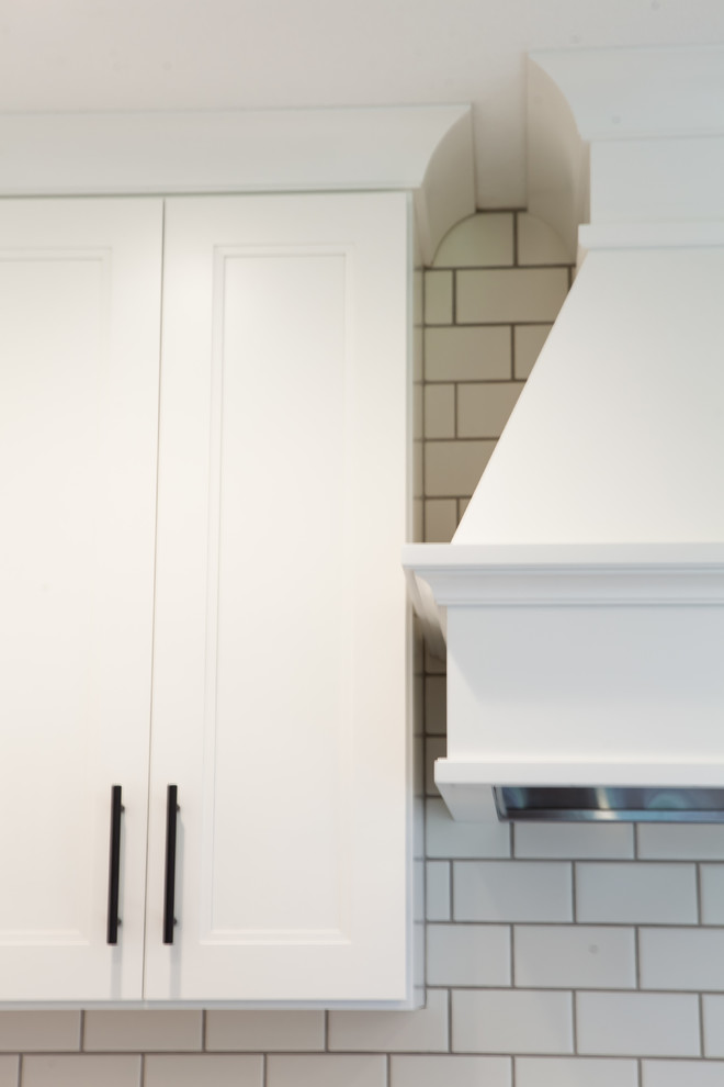 Large transitional l-shaped dark wood floor and brown floor home design photo with an undermount sink, recessed-panel cabinets, white cabinets, quartz countertops, white backsplash, subway tile backsplash, stainless steel appliances and an island