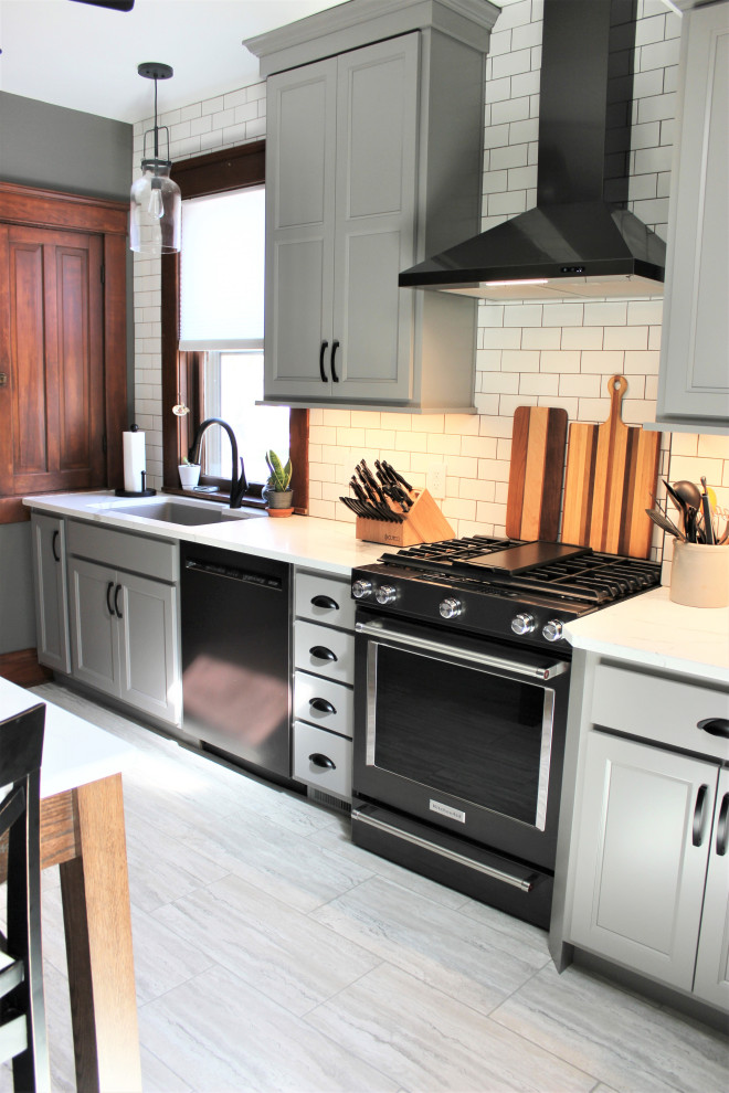Klassisk inredning av ett avskilt, mellanstort vit vitt l-kök, med en undermonterad diskho, släta luckor, grå skåp, bänkskiva i kvarts, vitt stänkskydd, stänkskydd i tunnelbanekakel, svarta vitvaror, vinylgolv, en köksö och grått golv