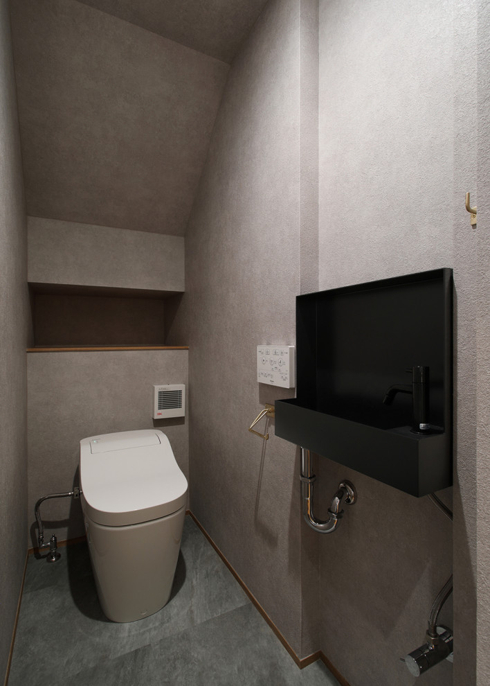 Photo of a small scandi cloakroom in Other with black cabinets, a one-piece toilet, grey tiles, grey walls, porcelain flooring, a wall-mounted sink, solid surface worktops, grey floors, black worktops, a feature wall, a built in vanity unit, a wallpapered ceiling and wallpapered walls.