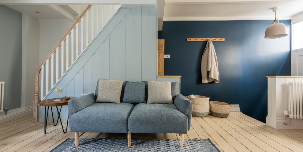 Пример оригинального дизайна: маленькая открытая гостиная комната в скандинавском стиле с синими стенами, светлым паркетным полом, стандартным камином, фасадом камина из металла, отдельно стоящим телевизором, балками на потолке и акцентной стеной для на участке и в саду