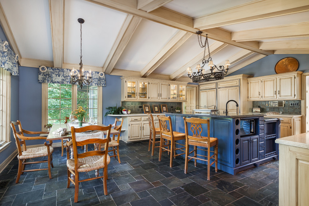 Photo of a large country l-shaped eat-in kitchen in Chicago with a farmhouse sink, glass-front cabinets, blue cabinets, quartz benchtops, blue splashback, slate splashback, stainless steel appliances, slate floors and with island.