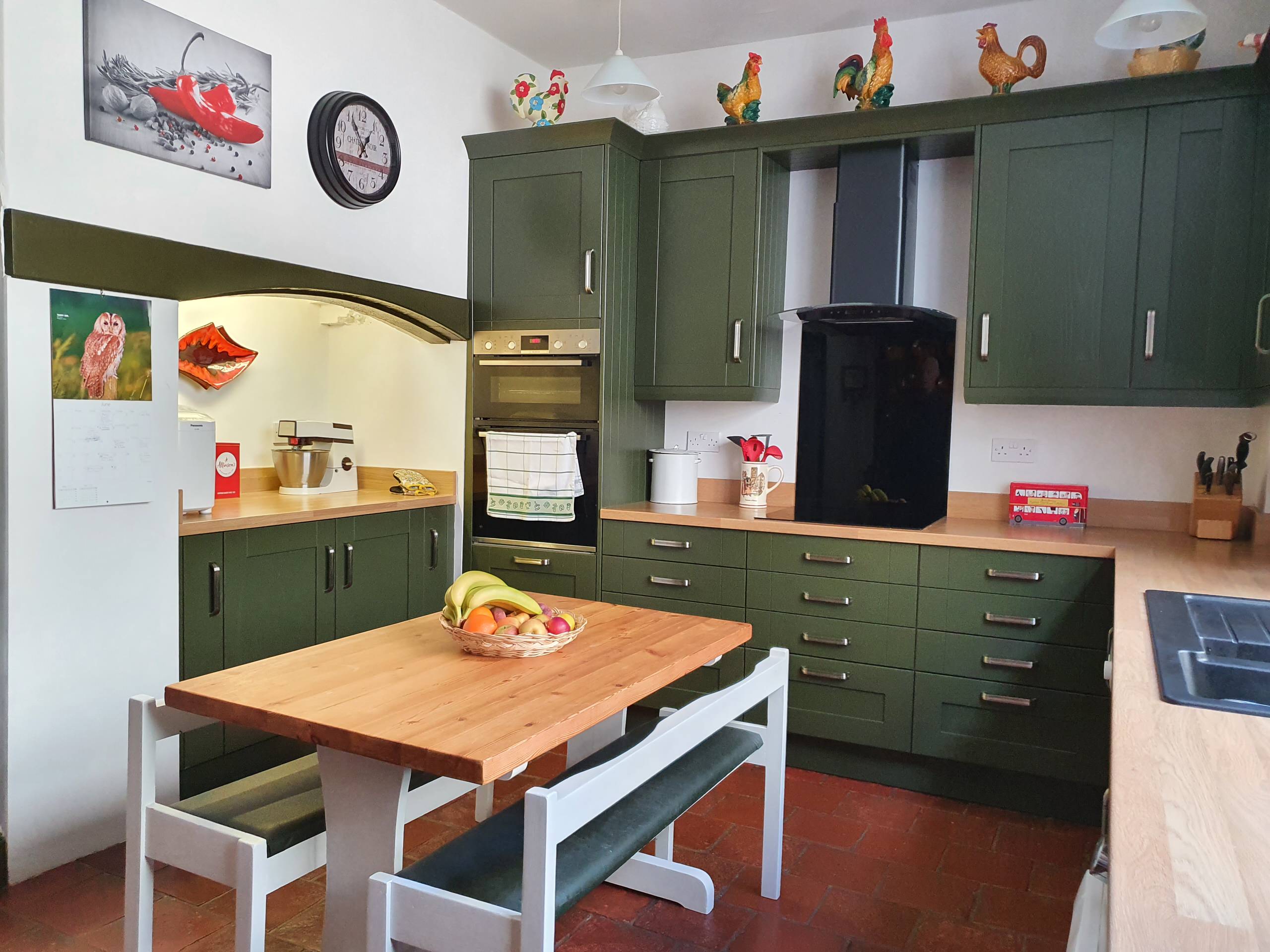 Cucina in bianco e marrone, con pavimento in piastrelle di terracotta,  unità cassetto al di sotto del piano di cottura e tavolo da pranzo con  porta aperta sul giardino Foto stock 