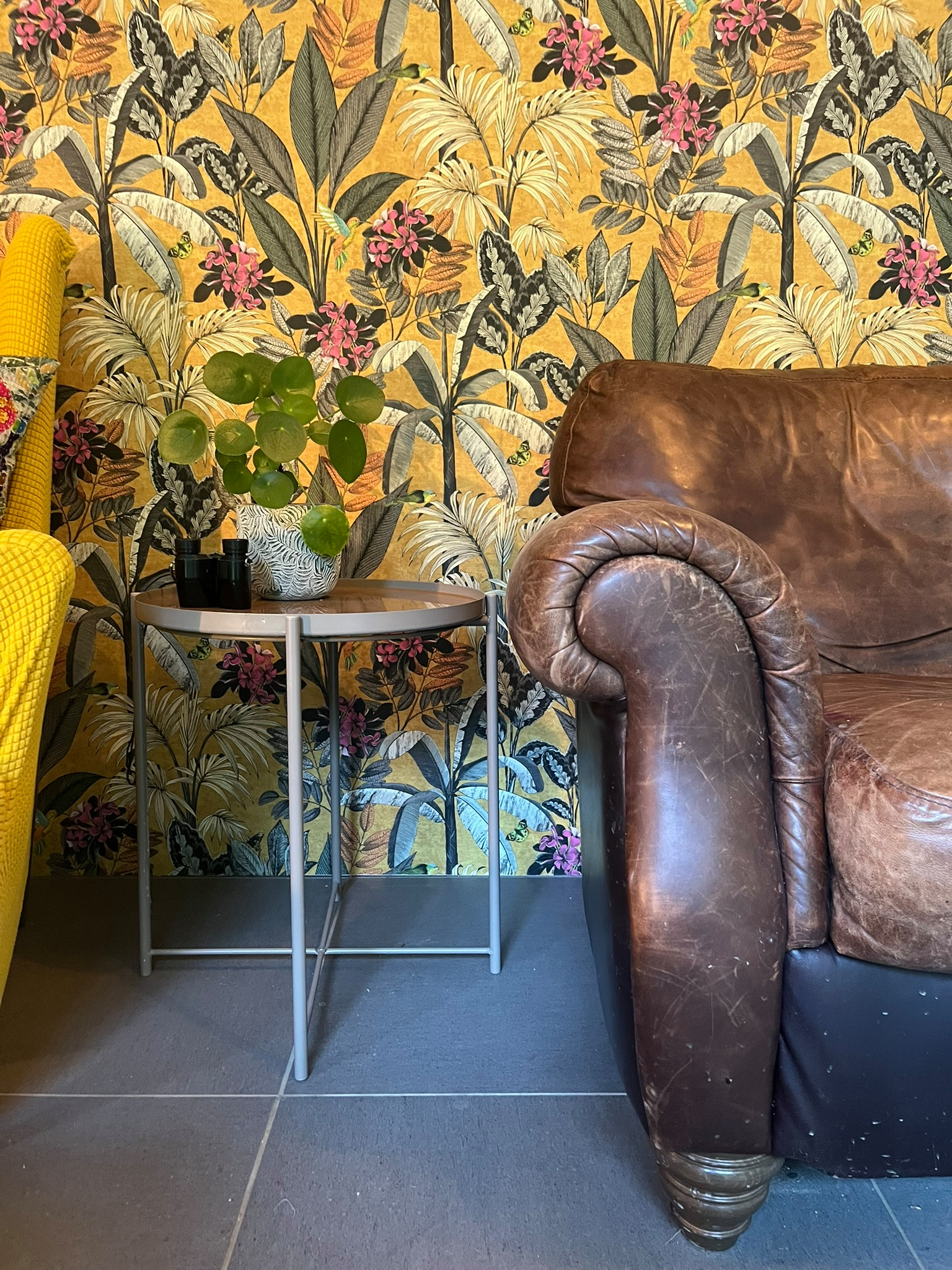 This room blends eclectic charm with a cozy, lived-in warmth. A bold botanical feature wall sets the tone, creating a lush backdrop for the rich, weathered leather sofa and the mix of vintage wooden p