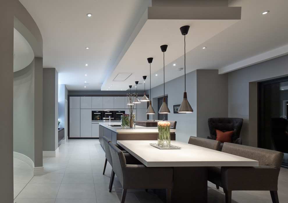 Photo of an expansive contemporary single-wall open plan kitchen with flat-panel cabinets, composite countertops, porcelain flooring, an island, grey walls, white cabinets, stainless steel appliances, grey floors and white worktops.