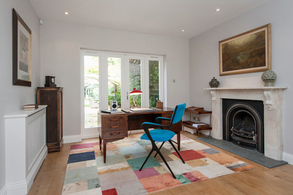 This is an example of a classic study in London with grey walls, light hardwood flooring, a standard fireplace and a freestanding desk.