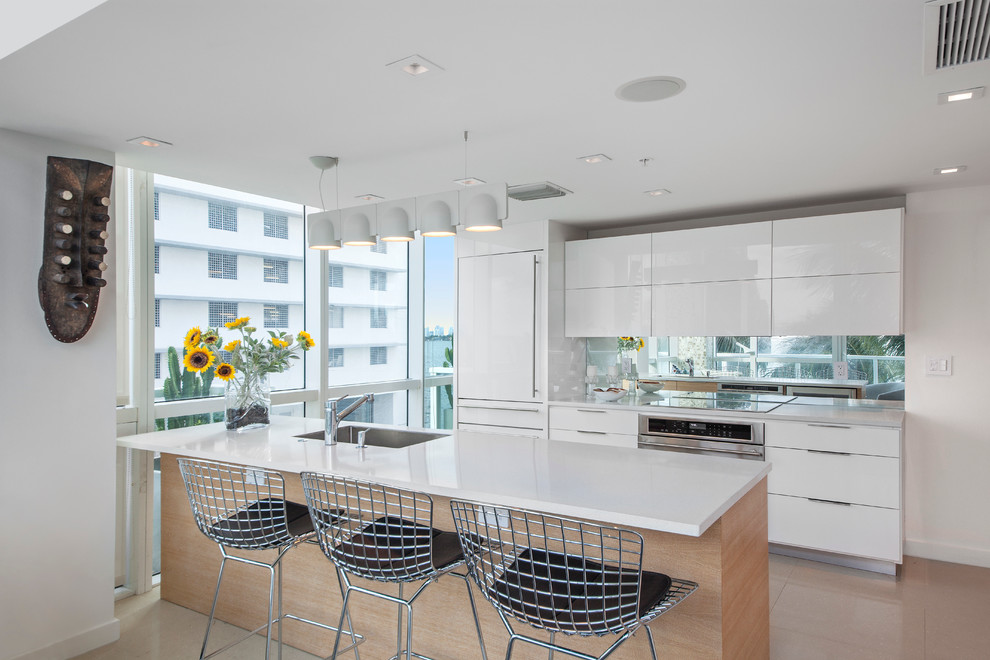 Contemporary galley open plan kitchen in Miami with white cabinets, mirror splashback, flat-panel cabinets, panelled appliances and a peninsula.