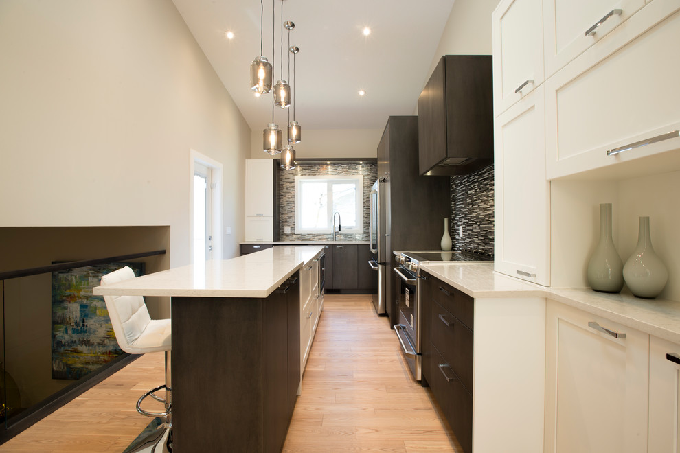 Example of a mid-sized transitional l-shaped light wood floor eat-in kitchen design in Calgary with an undermount sink, shaker cabinets, white cabinets, quartzite countertops, gray backsplash, ceramic backsplash, stainless steel appliances and an island