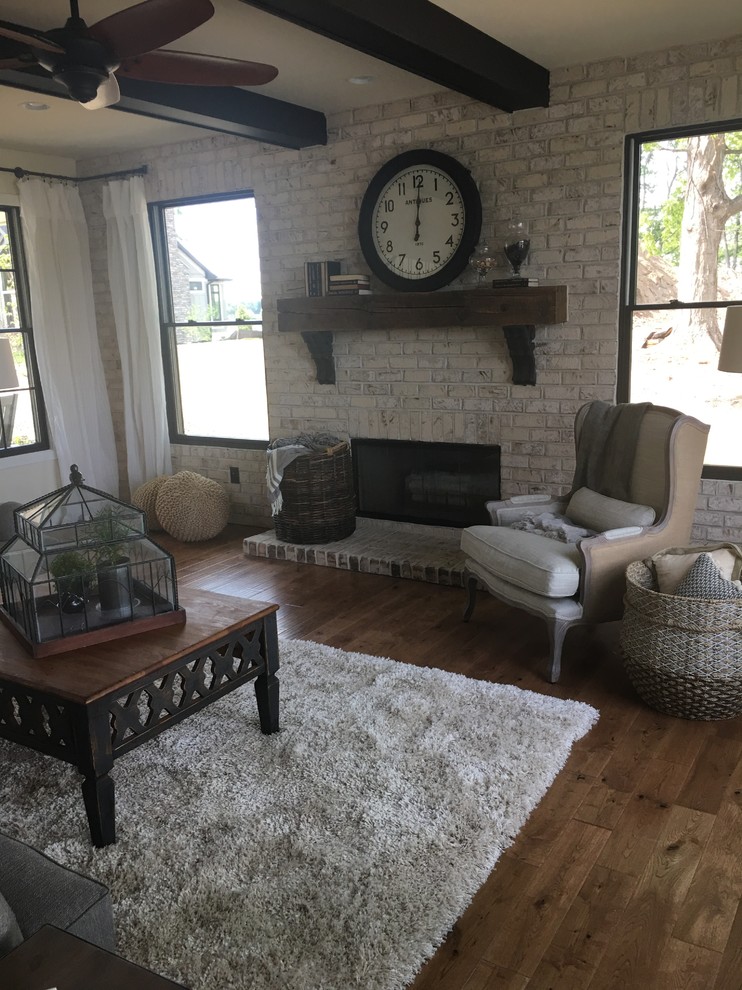 This is an example of a mid-sized country living room in Grand Rapids with white walls, medium hardwood floors, a brick fireplace surround and brown floor.