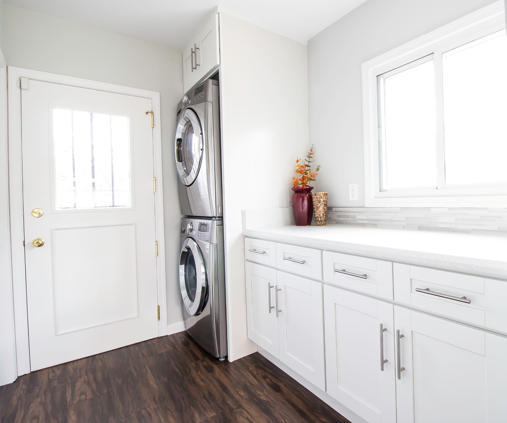 Photo of a mid-sized contemporary single-wall utility room in Los Angeles with recessed-panel cabinets, white cabinets, quartz benchtops, grey walls, ceramic floors and a stacked washer and dryer.