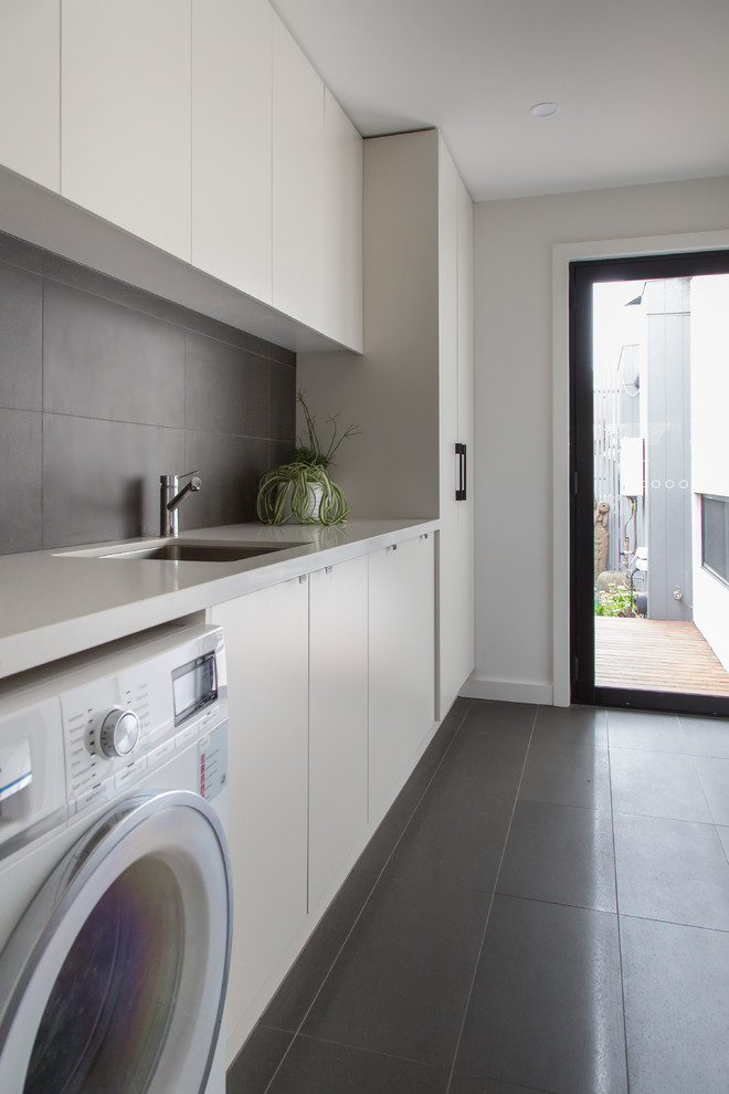 Photo of a mid-sized contemporary galley laundry room in Melbourne with a drop-in sink, shaker cabinets, white cabinets, quartz benchtops, white walls, concrete floors, a side-by-side washer and dryer, grey floor and white benchtop.