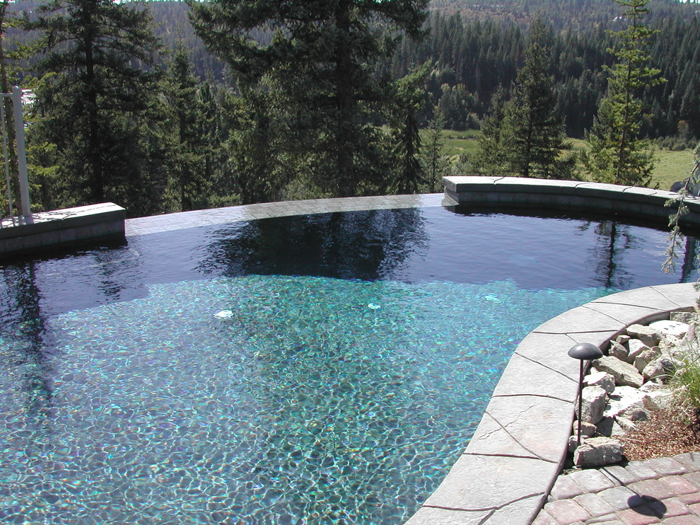 Inspiration for a large traditional backyard custom-shaped infinity pool in Seattle with natural stone pavers.