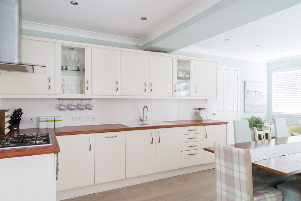 Photo of a mid-sized modern l-shaped eat-in kitchen in Other with a drop-in sink, glass-front cabinets, beige cabinets, laminate benchtops, beige splashback, ceramic splashback, stainless steel appliances and no island.