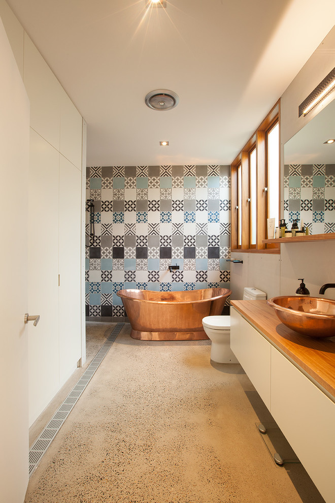 Mid-sized contemporary master bathroom in Sydney with white cabinets, wood benchtops, a freestanding tub, an open shower, multi-coloured tile, concrete floors, a one-piece toilet, cement tile, blue walls and a vessel sink.