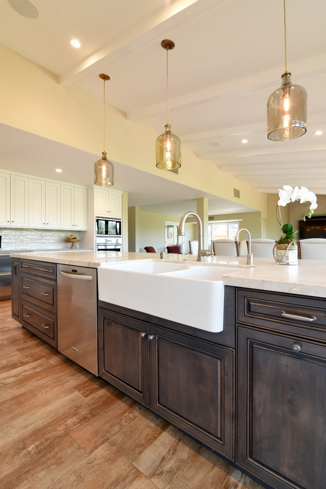 Inspiration for a large transitional l-shaped eat-in kitchen in Santa Barbara with a farmhouse sink, raised-panel cabinets, white cabinets, quartzite benchtops, beige splashback, glass tile splashback, stainless steel appliances, vinyl floors and with island.