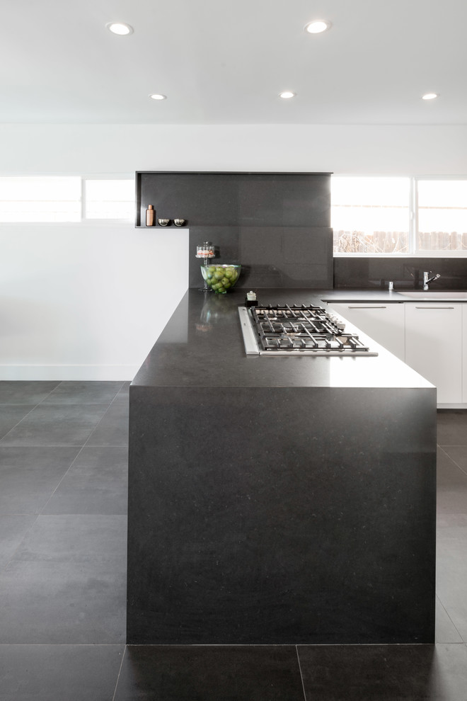 This is an example of a contemporary u-shaped eat-in kitchen in Los Angeles with an undermount sink, flat-panel cabinets, white cabinets, quartz benchtops, black splashback, panelled appliances and a peninsula.