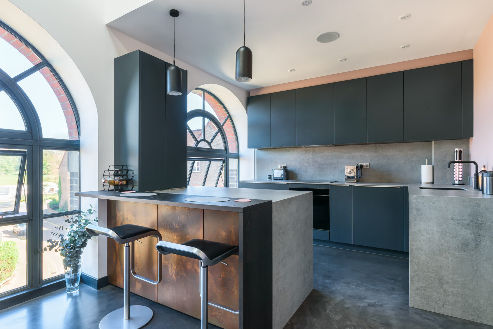 This is an example of a small contemporary l-shaped open plan kitchen in Sussex with with island, an undermount sink, flat-panel cabinets, black cabinets, concrete benchtops, grey splashback, cement tile splashback, panelled appliances, concrete floors, grey floor and grey benchtop.