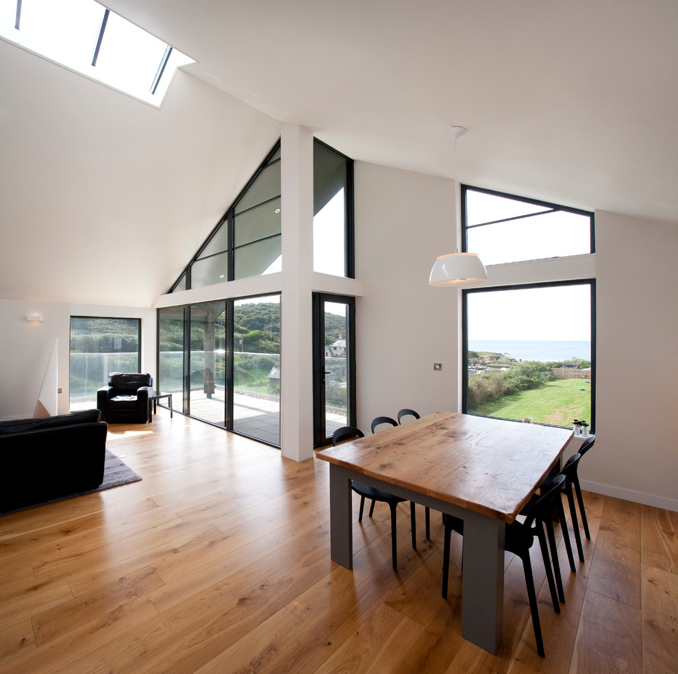This is an example of a medium sized coastal open plan living room in Cornwall with white walls, medium hardwood flooring, a wood burning stove, a plastered fireplace surround, brown floors and a vaulted ceiling.
