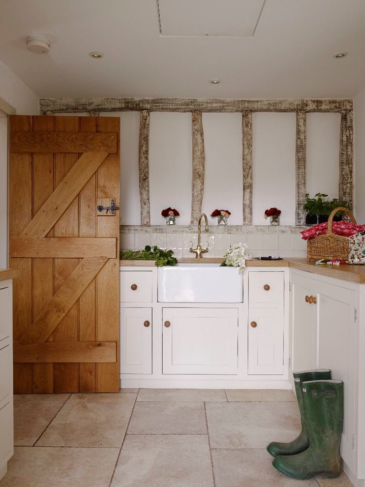 Design ideas for a mid-sized traditional galley laundry room in Hertfordshire with shaker cabinets, a farmhouse sink, white cabinets, wood benchtops and white walls.