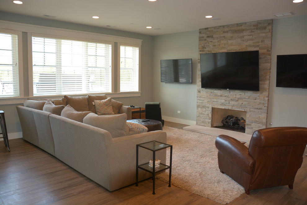 Photo of a large arts and crafts open concept family room in Chicago with grey walls, light hardwood floors, a standard fireplace, a stone fireplace surround, a wall-mounted tv and beige floor.