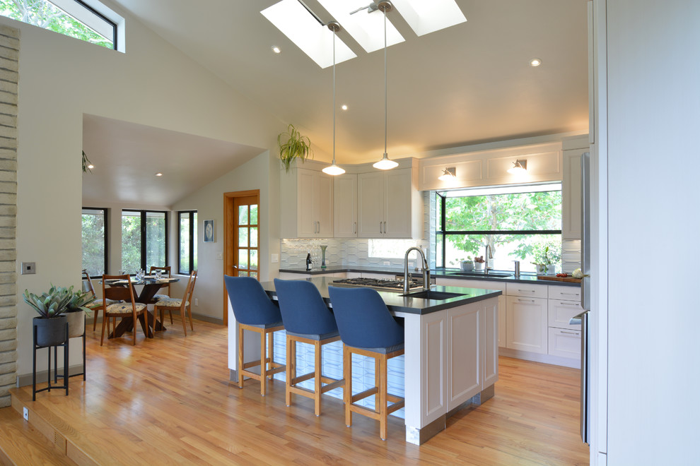 Design ideas for a large transitional u-shaped open plan kitchen in San Luis Obispo with an undermount sink, recessed-panel cabinets, white cabinets, quartz benchtops, white splashback, glass tile splashback, stainless steel appliances, light hardwood floors, with island, beige floor and grey benchtop.