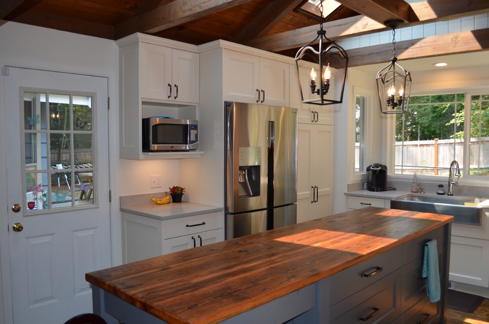 Inspiration for a mid-sized country u-shaped eat-in kitchen in Seattle with a farmhouse sink, shaker cabinets, white cabinets, quartz benchtops, white splashback, brick splashback, stainless steel appliances, medium hardwood floors, with island and brown floor.