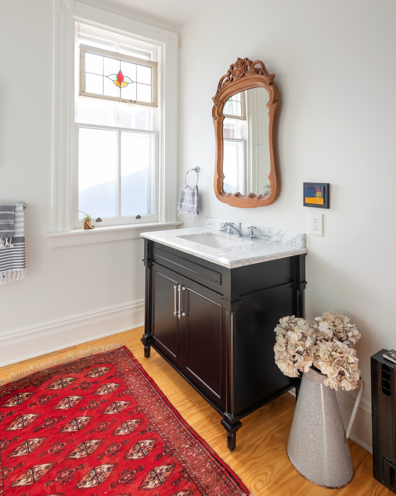 Bild på ett mellanstort vintage grå grått badrum med dusch, med släta luckor, svarta skåp, en toalettstol med separat cisternkåpa, vit kakel, keramikplattor, vita väggar, mellanmörkt trägolv, ett undermonterad handfat, marmorbänkskiva, brunt golv och dusch med gångjärnsdörr