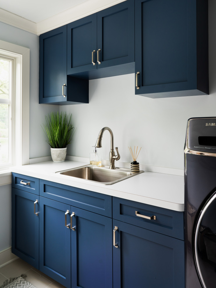 Inspiration for a mid-sized transitional single-wall laundry room in New York with a drop-in sink, shaker cabinets, blue cabinets, grey walls, a side-by-side washer and dryer and white benchtop.