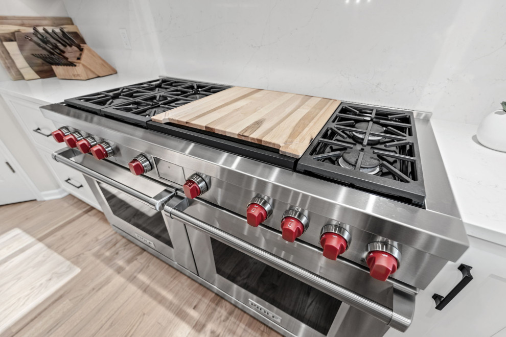 Eat-in kitchen - large transitional u-shaped light wood floor and multicolored floor eat-in kitchen idea with a single-bowl sink, shaker cabinets, white cabinets, quartz countertops, white backsplash, quartz backsplash, stainless steel appliances, an island and white countertops