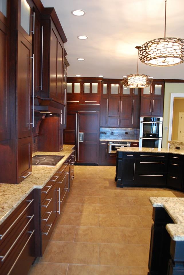 Design ideas for a large traditional u-shaped eat-in kitchen in Chicago with an undermount sink, raised-panel cabinets, dark wood cabinets, granite benchtops, multi-coloured splashback, travertine splashback, stainless steel appliances, medium hardwood floors, with island, brown floor and brown benchtop.
