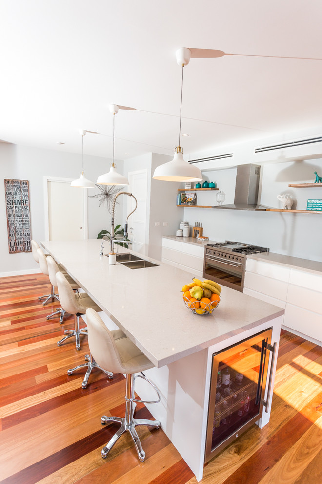 Expansive contemporary galley kitchen pantry in Sydney with an undermount sink, flat-panel cabinets, white cabinets, quartz benchtops, grey splashback, glass sheet splashback, stainless steel appliances, medium hardwood floors and with island.