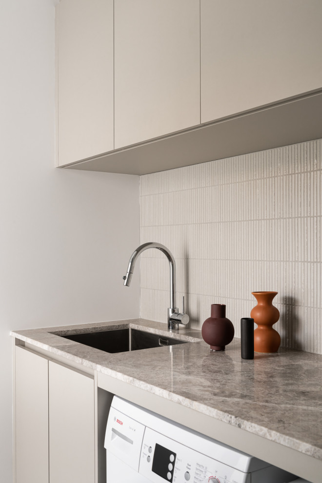 Design ideas for a mid-sized modern single-wall dedicated laundry room in Perth with an undermount sink, beige cabinets, marble benchtops, beige splashback, mosaic tile splashback, white walls, porcelain floors, a side-by-side washer and dryer and grey floor.