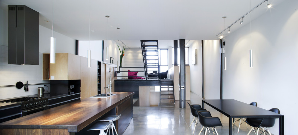 Modern galley eat-in kitchen in Montreal with wood benchtops, black cabinets and white splashback.