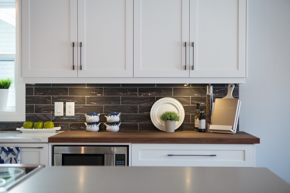 Example of a mid-sized arts and crafts l-shaped medium tone wood floor and brown floor kitchen design with shaker cabinets, white cabinets, wood countertops, subway tile backsplash, stainless steel appliances, a double-bowl sink, brown backsplash and an island