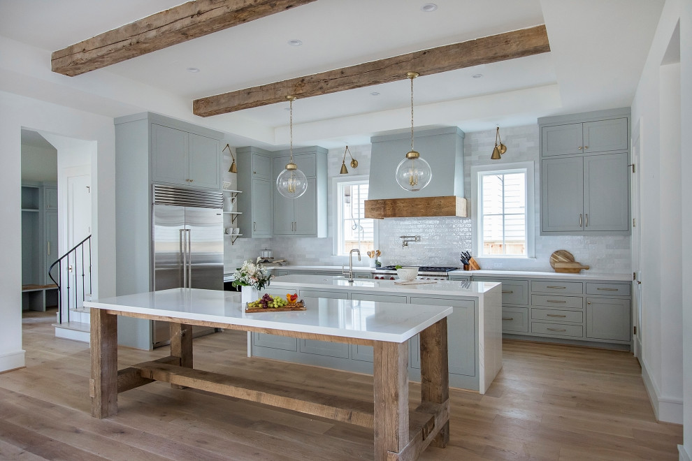 Inspiration for a farmhouse l-shaped medium tone wood floor and brown floor eat-in kitchen remodel in Houston with a farmhouse sink, shaker cabinets, gray cabinets, white backsplash, subway tile backsplash, an island and white countertops