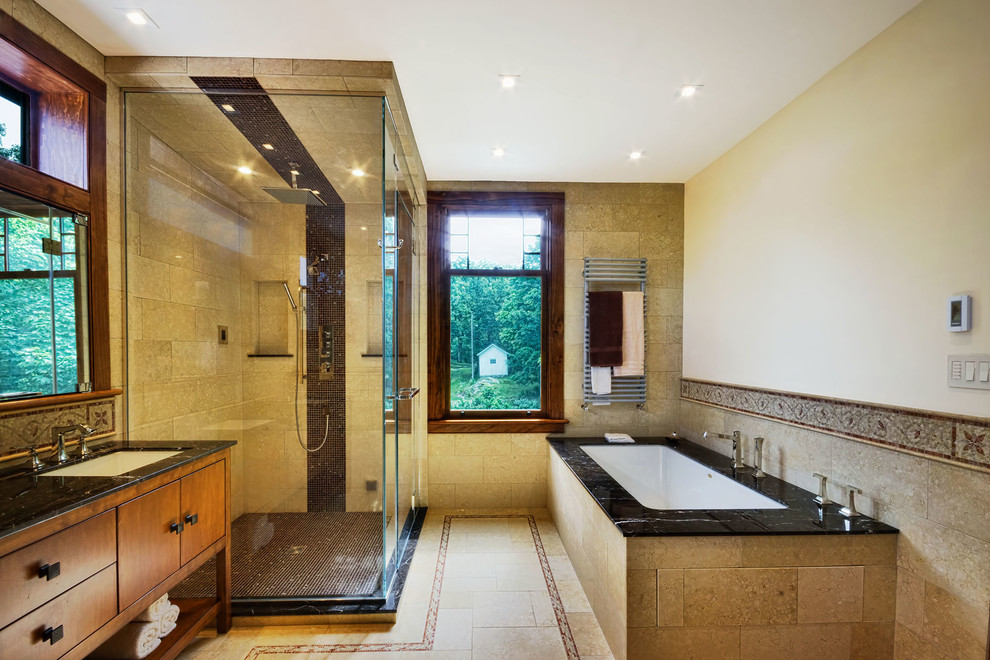 This is an example of a large modern master bathroom in New York with an undermount sink, furniture-like cabinets, medium wood cabinets, marble benchtops, an undermount tub, a two-piece toilet, brown tile, stone tile, brown walls and limestone floors.