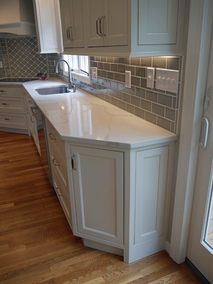 This is an example of a mid-sized transitional l-shaped eat-in kitchen in Boston with an undermount sink, beaded inset cabinets, white cabinets, quartz benchtops, grey splashback, porcelain splashback, stainless steel appliances, medium hardwood floors, with island and red floor.
