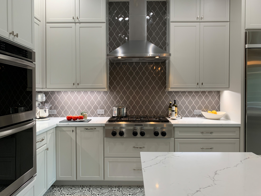 Inspiration for a transitional l-shaped porcelain tile and multicolored floor kitchen remodel in Houston with a farmhouse sink, recessed-panel cabinets, white cabinets, quartz countertops, gray backsplash, ceramic backsplash, stainless steel appliances, an island and white countertops