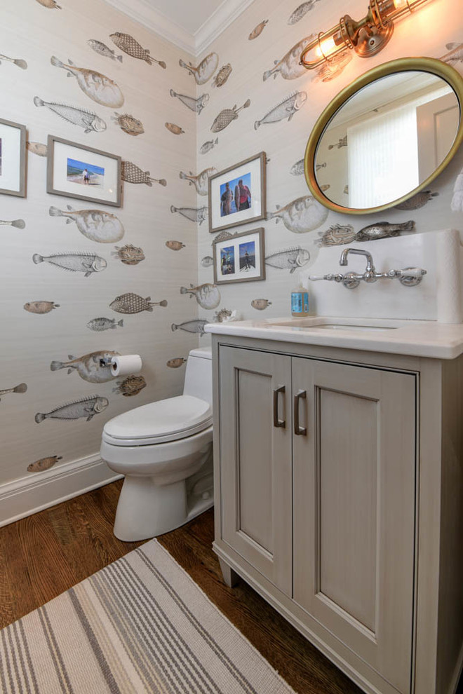 This is an example of a mid-sized beach style powder room in New Orleans with beaded inset cabinets, brown cabinets, multi-coloured walls, medium hardwood floors, an undermount sink, brown floor, a one-piece toilet and solid surface benchtops.