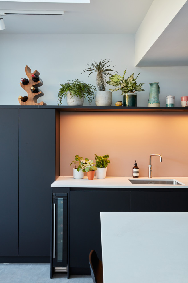 Inspiration for a medium sized modern u-shaped kitchen/diner in London with an integrated sink, flat-panel cabinets, black cabinets, engineered stone countertops, pink splashback, glass sheet splashback, stainless steel appliances, an island and white worktops.